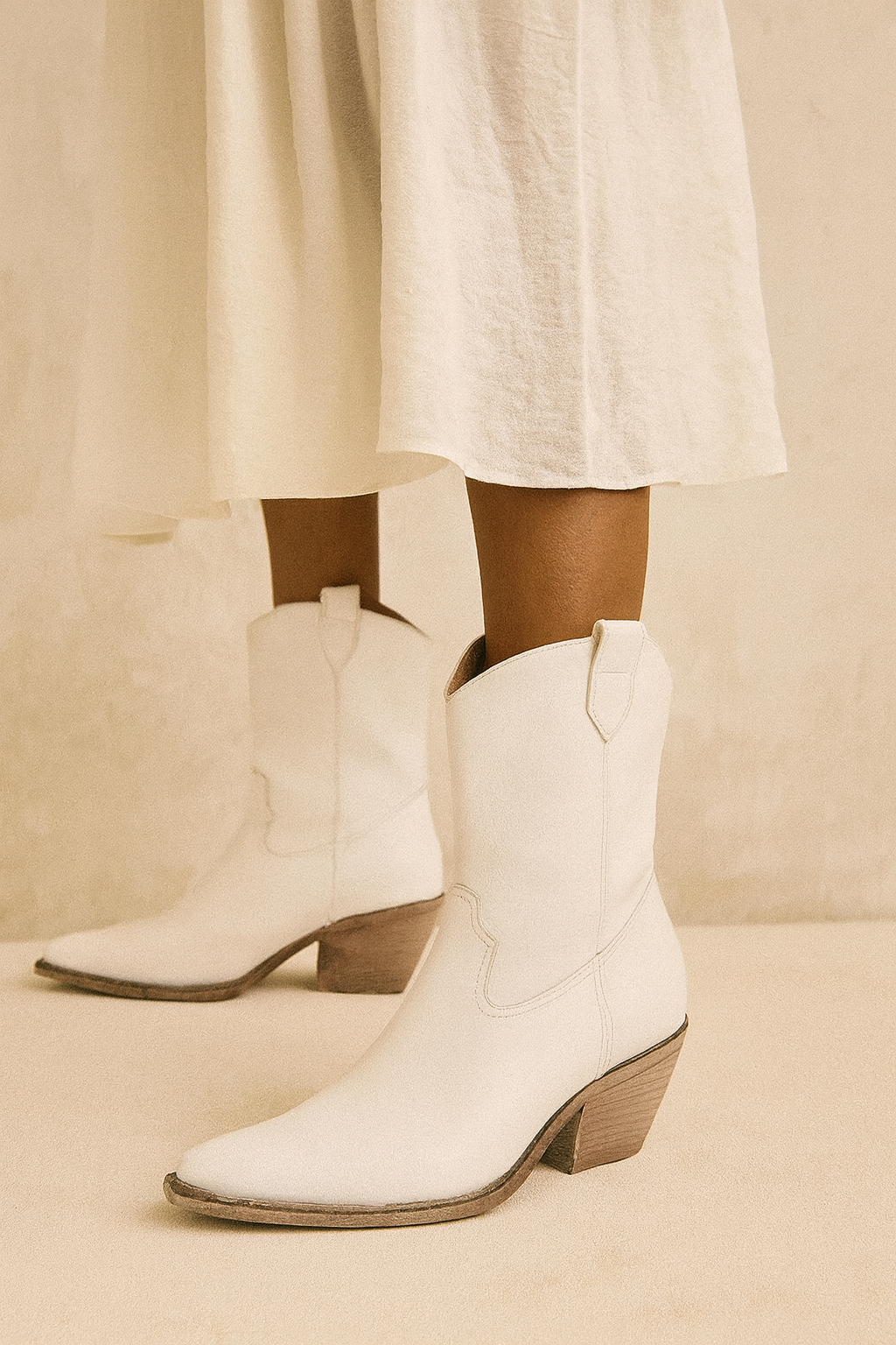 White cowboy boots worn with a white skirt on a beige background
