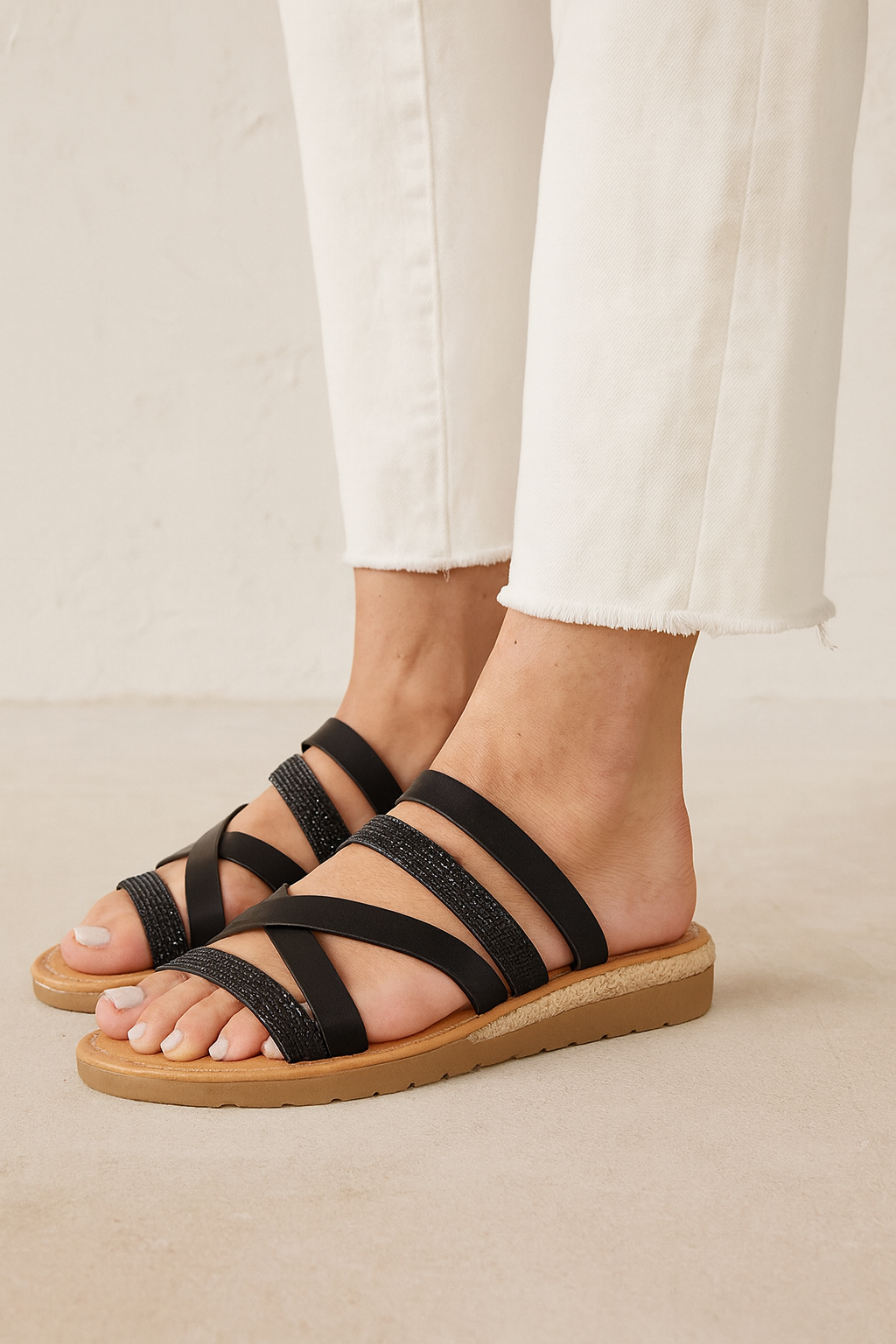 Black strappy sandals worn with white pants on a neutral background