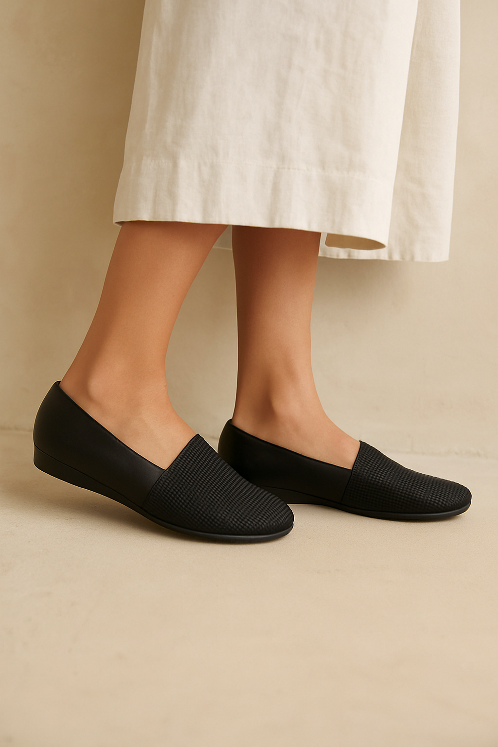 Black slip-on shoes worn with a white skirt on a beige background