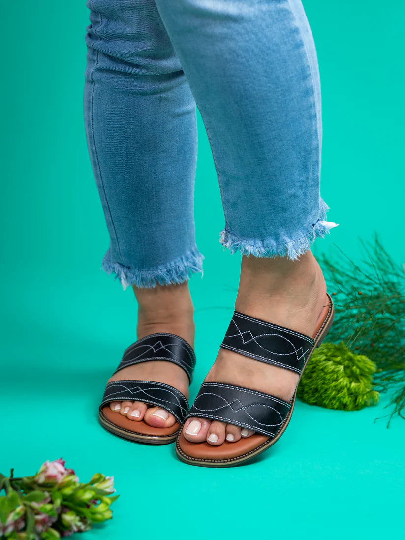 Black sandals worn with light blue jeans on a green background