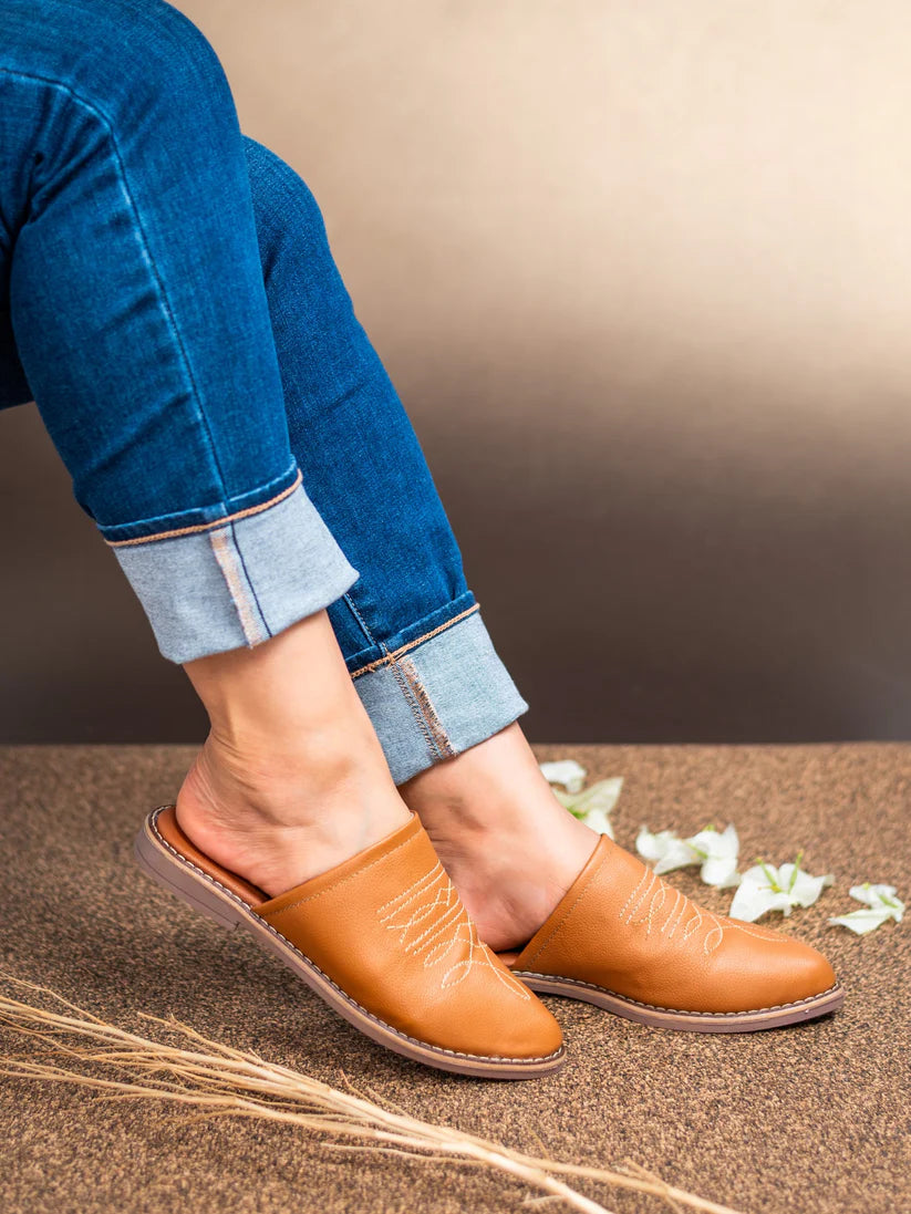 Person wearing brown leather shoes and blue jeans on a neutral background