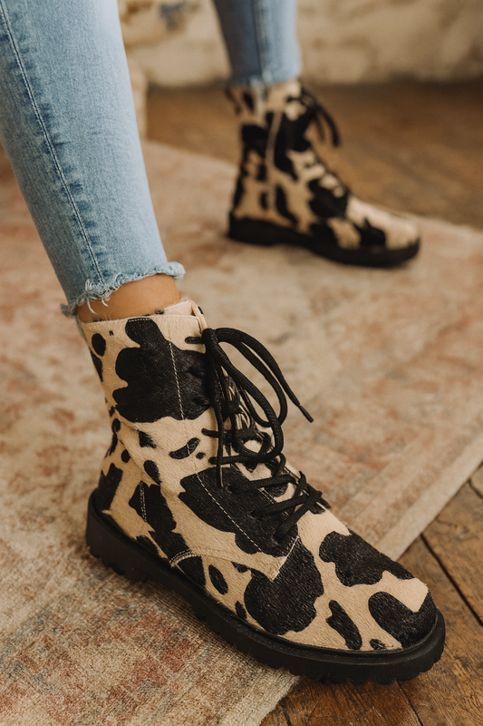 Cow print boots worn with light blue jeans on a wooden floor.